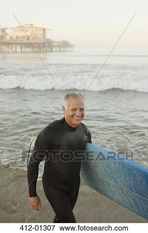 Older surfer carrying board on beach View Large Photo Image Stock Photo - Older surfer carrying board on beach. Fotosearch