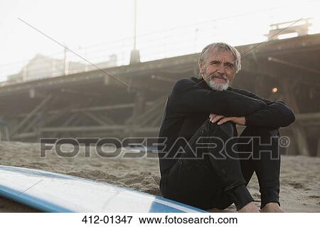 Stock Photo - Older surfer sitting with board on beach. Fotosearch