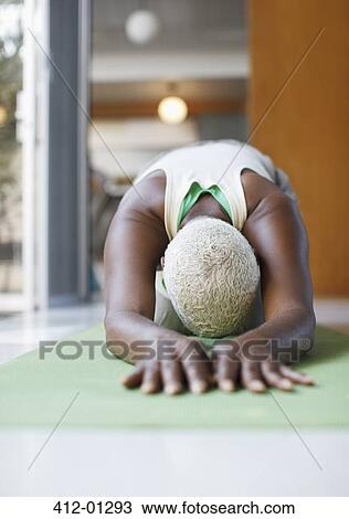 Stock Image - Older woman practicing yoga in living room. Fotosearch