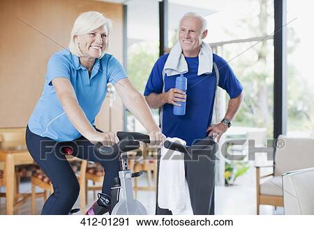Stock Image - Older woman riding exercise bike at home. Fotosearch