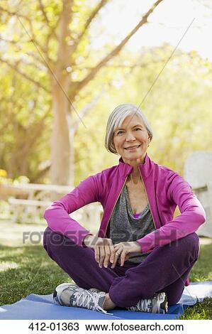 Stock Image - Older woman sitting on yoga mat outdoors. Fotosearch
