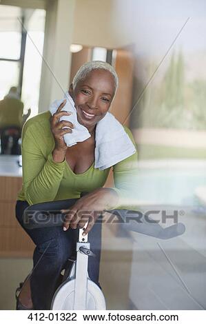 Stock Image - Older woman using exercise bike in home. Fotosearch