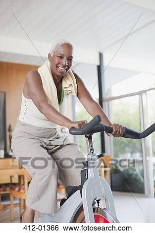 Stock Photograph - Older woman using exercise bike in home. Fotosearch