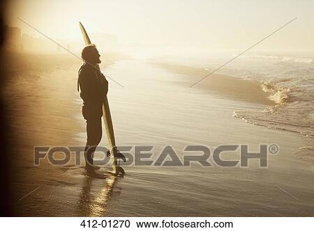 Surfer standing with board on beach View Large Photo Image Stock Image - Surfer standing with board on beach. Fotosearch