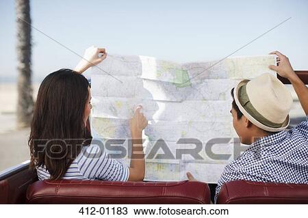 Stock Image - Couple reading road map in convertible. Fotosearch