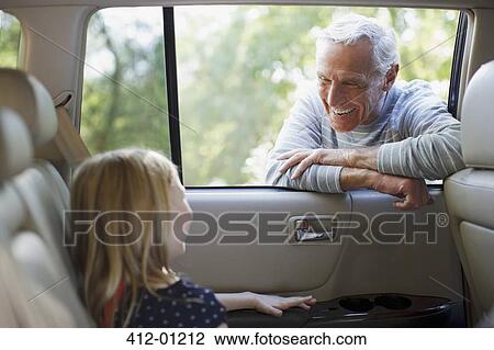 Stock Image - Older man talking to granddaughter in car window. Fotosearch