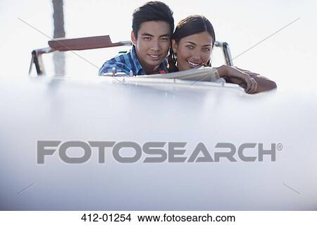 Picture - Smiling couple sitting in convertible. Fotosearch