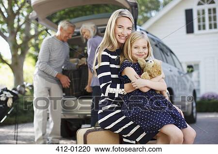 Stock Image - Smiling mother and daughter sitting on luggage. Fotosearch