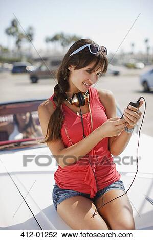Stock Image - Smiling woman listening to mp3 player on car. Fotosearch