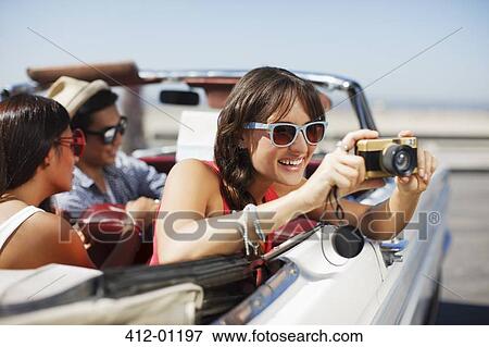 Stock Photo - Smiling woman taking picture from convertible. Fotosearch