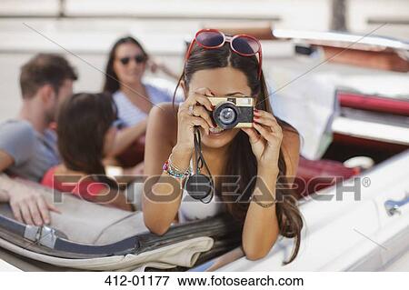 Woman taking picture from convertible View Large Photo Image Stock Photo - Woman taking picture from convertible. Fotosearch