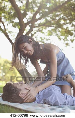 Stock Photograph - Affectionate couple on blanket in grass under tree. Fotosearch
