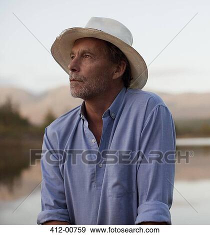 Stock Photo - Close up of pensive man in hat at lakeside. Fotosearch