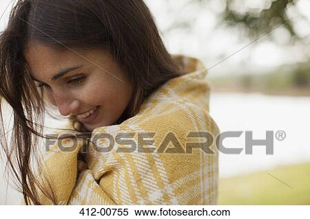 Stock Photography - Close up of smiling woman wrapped in blanket at lakeside. Fotosearch