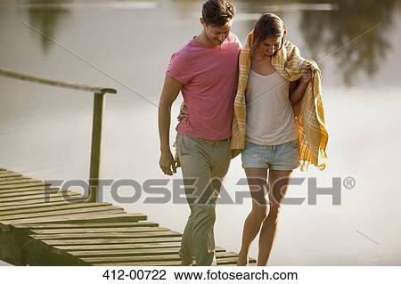 Stock Image - Couple walking on dock over lake. Fotosearch