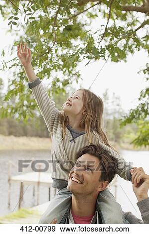 Daughter on father's shoulders reaching for branc View Large Photo Image Stock Photo - Daughter on father's shoulders reaching for branc. Fotosearch