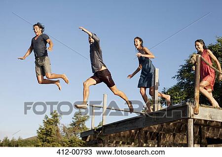 Stock Image - Enthusiastic friends jumping off dock. Fotosearch