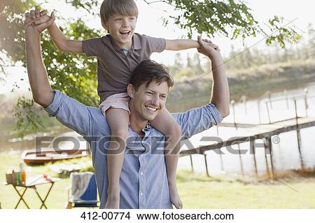 Father carrying smiling son on shoulders at lakeside View Large Photo Image Picture - Father carrying smiling son on shoulders at lakeside. Fotosearch