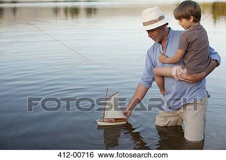 Grandfather and grandson wading in lake with toy sailboat View Large Photo Image Stock Photograph - Grandfather and grandson wading in lake with toy sailboat. Fotosearch