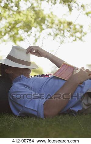 Picture - Man napping in grass with book and hat covering face. Fotosearch