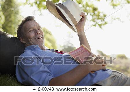 Portrait of smiling man laying on grass with book and hat View Large Photo Image Stock Image - Portrait of smiling man laying on grass with book and hat. Fotosearch