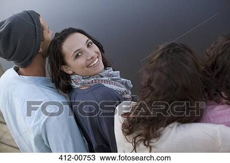 Stock Image - Portrait of smiling woman sitting with friends at lake. Fotosearch