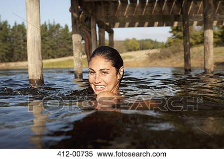 Stock Photography - Portrait of smiling woman swimming in lake under dock. Fotosearch