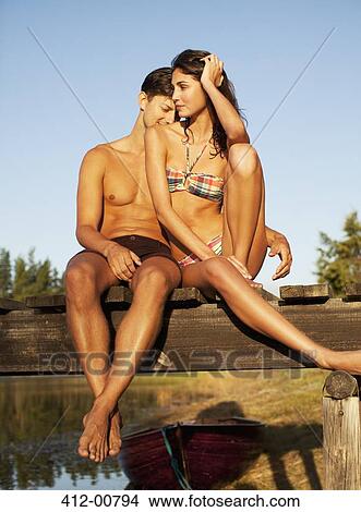 Serene couple sitting at edge of dock over lake View Large Photo Image Picture - Serene couple sitting at edge of dock over lake. Fotosearch