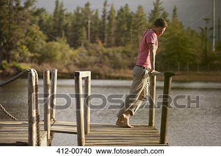 Serene man standing at railing of dock over lake View Large Photo Image Stock Image - Serene man standing at railing of dock over lake. Fotosearch