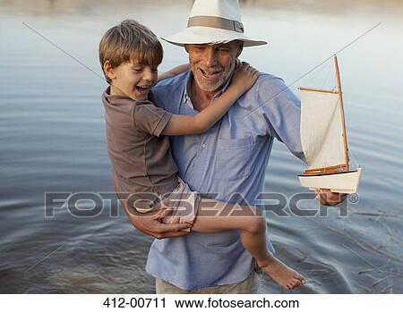 Smiling grandfather and grandson with toy sailboat wading in lake View Large Photo Image Stock Image - Smiling grandfather and grandson with toy sailboat wading in lake. Fotosearch