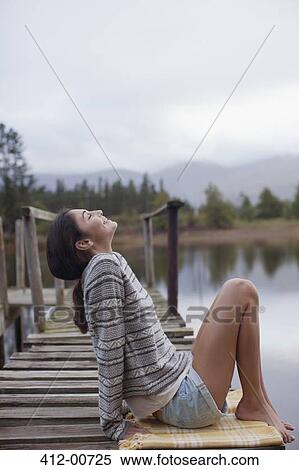 Smiling woman sitting on dock at lakeside with head back View Large Photo Image Stock Photography - Smiling woman sitting on dock at lakeside with head back. Fotosearch