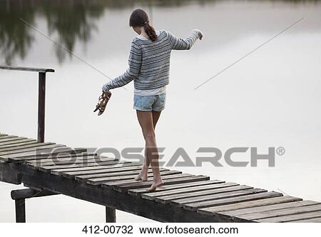 Stock Image - Woman walking along dock over lake. Fotosearch