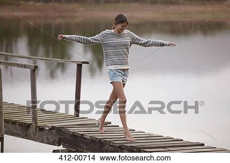 Picture - Woman walking on dock over lake with arms outstretched. Fotosearch