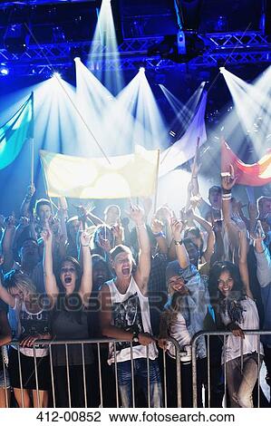 Crowd cheering with arms raised behind railing at concert View Large Photo Image Stock Image - Crowd cheering with arms raised behind railing at concert. Fotosearch