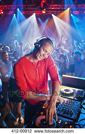 Stock Image - DJ at turntable with crowd on dance floor in background. Fotosearch