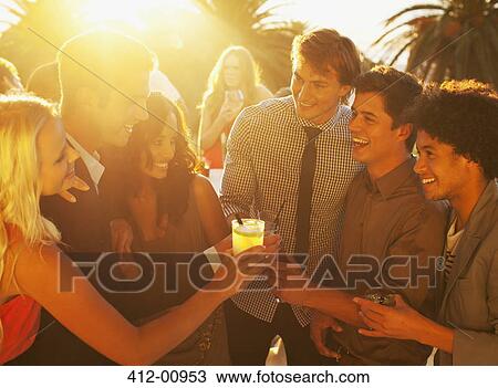 Stock Image - Friends toasting cocktails on sunny balcony. Fotosearch