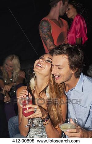 Stock Photo - Laughing couple hugging and drinking cocktails in nightclub. Fotosearch