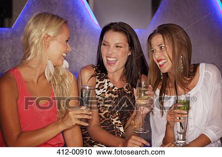 Stock Image - Laughing women drinking cocktails in nightclub. Fotosearch
