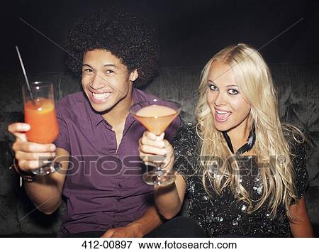 Stock Photo - Portrait of enthusiastic couple toasting cocktails in nightclub. Fotosearch
