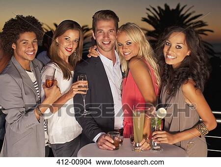 Picture - Portrait of smiling friends drinking cocktails on balcony at sunset. Fotosearch