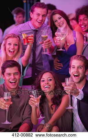 Stock Image - Portrait of smiling friends drinking cocktails in nightclub. Fotosearch