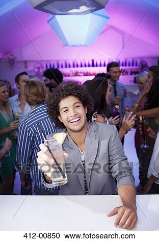 Stock Image - Portrait of smiling man holding cocktail at bar of nightclub. Fotosearch