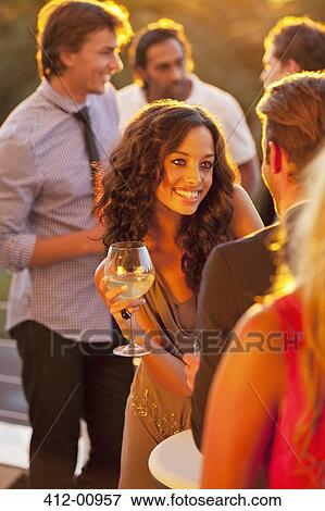 Stock Photo - Smiling woman with wine glass talking to man on sunny balcony. Fotosearch