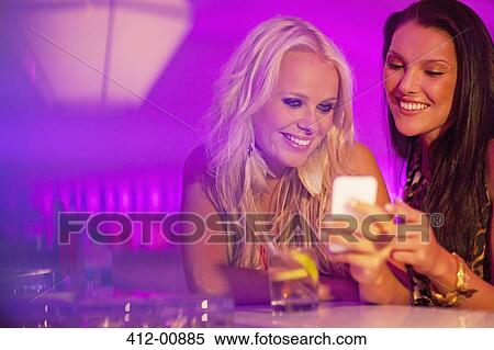 Stock Photography - Smiling women looking down at cell phone in nightclub. Fotosearch