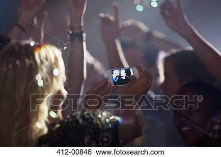 Stock Photograph - Woman with camera phone photographing friends on dance floor of nightclub. Fotosearch