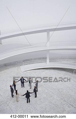 Business people holding hands and standing in circle in modern courtyard View Large Photo Image Stock Image - Business people holding hands and standing in circle in modern courtyard. Fotosearch