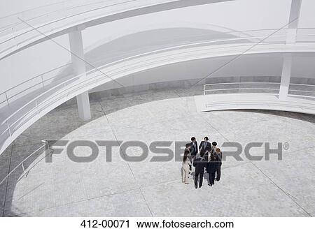 Stock Image - Business people standing in circle of modern courtyard. Fotosearch