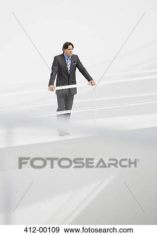 Stock Photo - Businessman leaning on railing at elevated walkway. Fotosearch