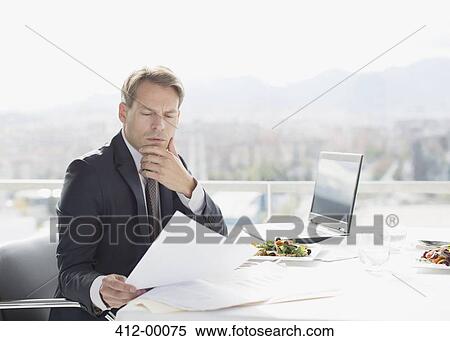 Stock Photography - Businessman with lunch reviewing paperwork. Fotosearch