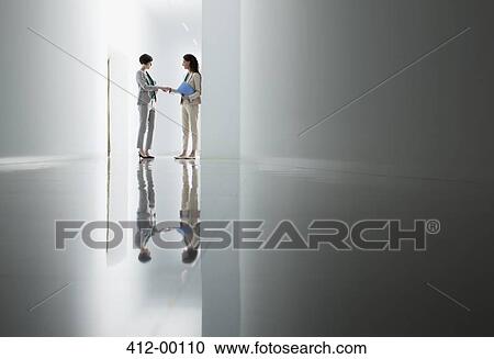 Stock Image - Businesswomen shaking hands in corridor. Fotosearch